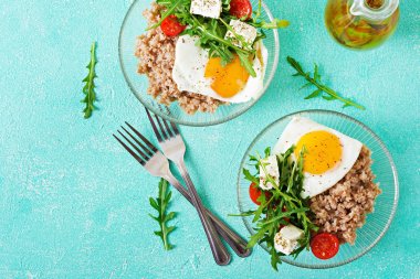 Sağlıklı kahvaltı yumurta, beyaz peynir, roka, domates ve buğday lapası ışık arka plan üzerinde. Doğru beslenme. Diyet menüsü. Düz yatıyordu. Üstten Görünüm