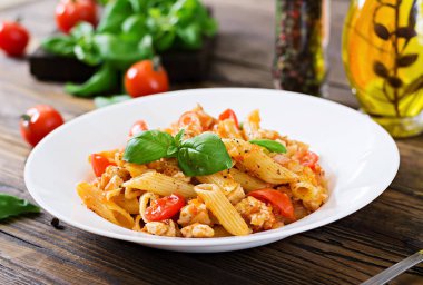 Penne makarna domates soslu tavuk, domates, fesleğen ahşap bir masa üzerinde ile dekore edilmiştir. İtalyan yemeği. Bolognese makarna.