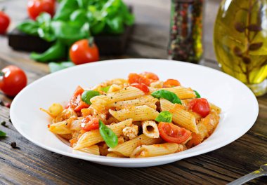 Penne makarna domates soslu tavuk, domates, fesleğen ahşap bir masa üzerinde ile dekore edilmiştir. İtalyan yemeği. Bolognese makarna.