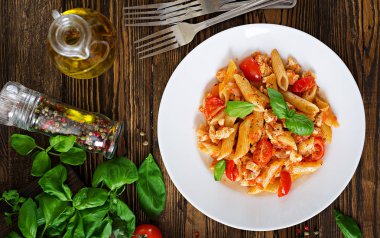 Ana sayfa görünümü Penne makarna domates soslu tavuk, domates, fesleğen ahşap bir masa üzerinde ile dekore edilmiştir. İtalyan yemeği. Bolognese makarna. Üstten Görünüm. Düz yatıyordu