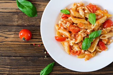 Ana sayfa görünümü Penne makarna domates soslu tavuk, domates, fesleğen ahşap bir masa üzerinde ile dekore edilmiştir. İtalyan yemeği. Bolognese makarna. 