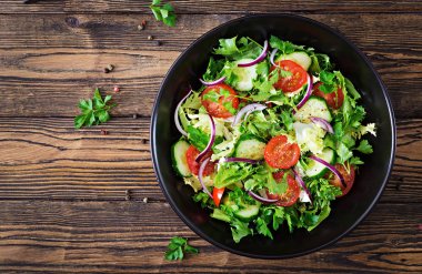 Yukarıdan vejetaryen salata domates, salatalık, kırmızı soğan ve marul yaprakları. Sağlıklı yaz vitamini menü. Vegan sebze gıda. Yemek Masası. Düz yatıyordu