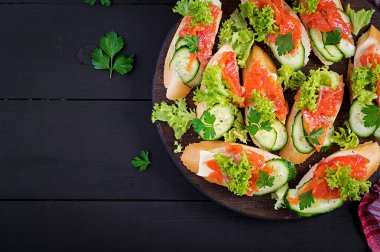 Tapas. Ahşap tahtada tuzlu somon, tereyağı ve salatalıklı tost sandviçleri. Üst görünüm