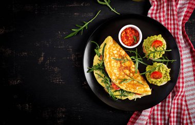 Kahvaltıda. Domatesli omlet, peynir, yeşil roka ve siyah tabakta avokado kremalı tost. Frittata - İtalyan omleti. Üst görünüm