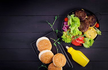 Hamburger pişirme. Büyük sandviç - hamburger, sığır eti, domates, peynir, salatalık turşusu ve kırmızı soğanlı. Üst görünüm