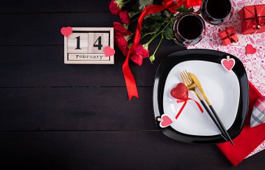 Sevgililer günü yemeği, hediye masası, kırmızı güller, koyu arkaplanda iki şarap kadehi olan kalpler. Üst manzara, düz uzanma.