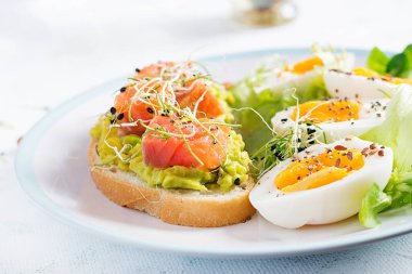 Kahvaltıda. Avokado ve somonlu sağlıklı bir sandviç haşlanmış yumurta, otlar, fotokopi alanı olan beyaz tabakta chia tohumları. Sağlıklı protein yiyeceği.