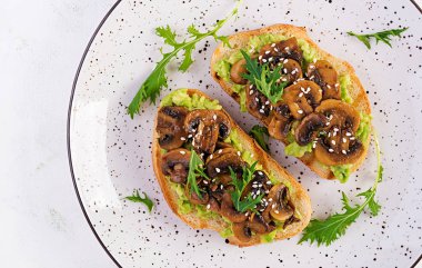 Allah 'ım. Avokadolu sandviç, kızarmış mantar, beyaz bir masada susam. Vejetaryen yemeği. Vejetaryen menüsü. Üst görünüm, genel görünüm