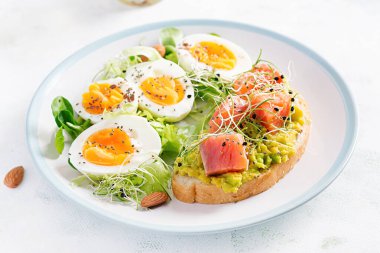 Kahvaltıda. Avokado ve somonlu sağlıklı bir sandviç haşlanmış yumurta, otlar, fotokopi alanı olan beyaz tabakta chia tohumları. Sağlıklı protein yiyeceği.