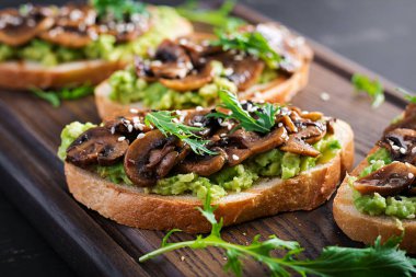 Allah 'ım. Avokado ile sandviç, kızarmış mantar, tahta tahtada susam. Vejetaryen yemeği. Vegan menüsü.