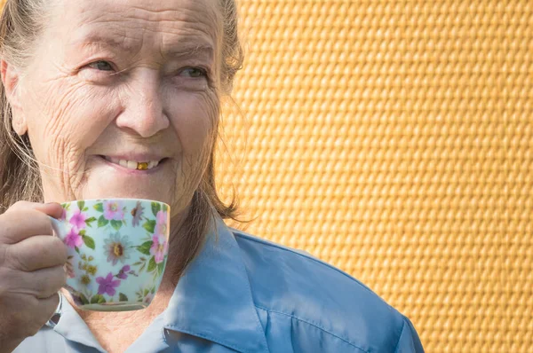 Портрет старой бабушки на открытом воздухе в солнечный день. Кавказская бабушка пьет горячий кофе, чай по утрам. пожилая женщина наслаждается завтраком, держа в руках теплую кружку, чашку. позитивная улыбка пожилой дамы — стоковое фото