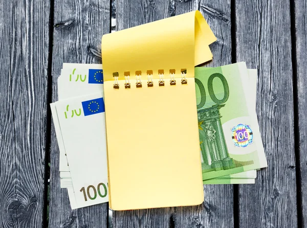 Honderd euro bankbiljetten en geel Kladblok — Stockfoto