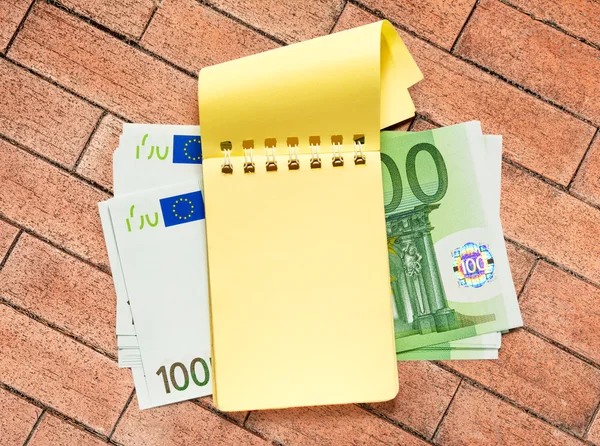 Honderd euro bankbiljetten en geel Kladblok — Stockfoto