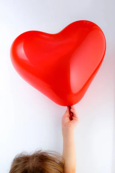 Красный сердечный шарик в детской руке — стоковое фото