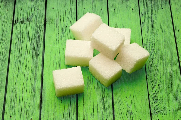 Sugar cubes on green wooden background — Stock Photo, Image