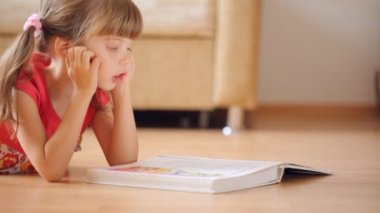 Küçük kız yerde yatarken kitap okur