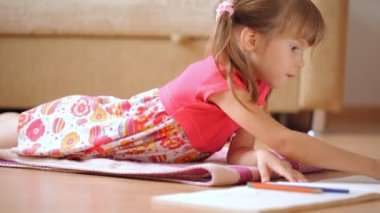 Küçük kız yerde yatarken resimler çizer