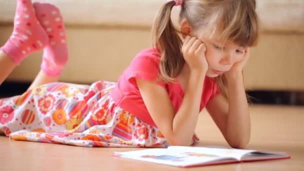 Маленькая Девочка Читает Книгу Лежащую Полу — стоковое видео