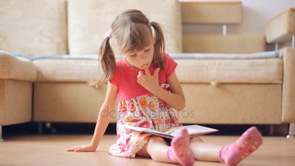 Маленькая Девочка Читает Книгу Сидя Полу — стоковое видео