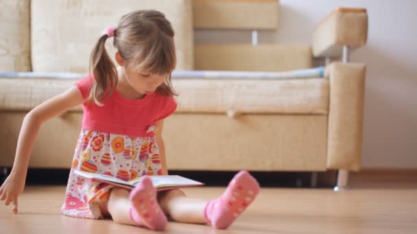 Маленька Дівчинка Читає Книгу Сидячи Підлозі — стокове відео