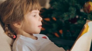 Küçük kız Noel ağacı önünde bir kitap okuma