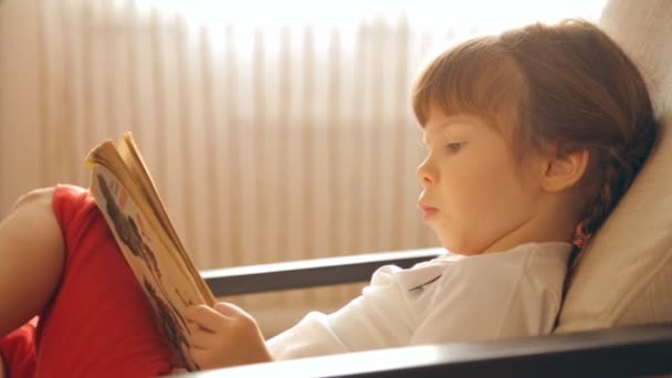 Маленькая Девочка Читает Книгу Кресле — стоковое видео
