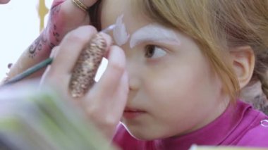 Sanatçı küçük kızın yüzünü boyuyor.