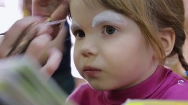 Sanatçı küçük kızın yüzünü boyuyor.