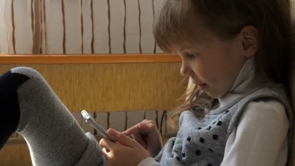 Маленька дівчинка зі смартфоном на дивані — стокове відео