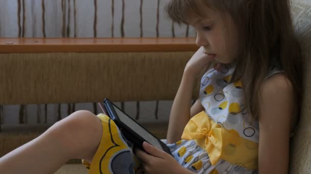 Petite fille lisant le livre électronique sur le canapé — Video