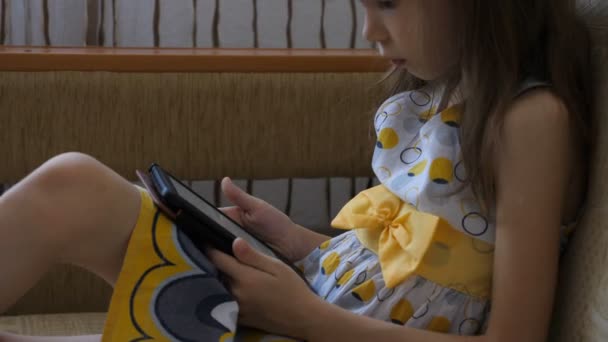 Klein meisje lezen elektronisch boek op de bank — Stockvideo