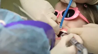 Dişçi koltuğundaki küçük kız dişini tedavi ettiriyor.