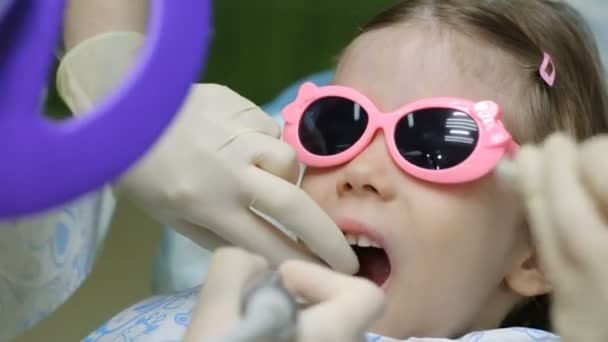Маленькой девочке в стоматологическом кресле лечат зуб — стоковое видео