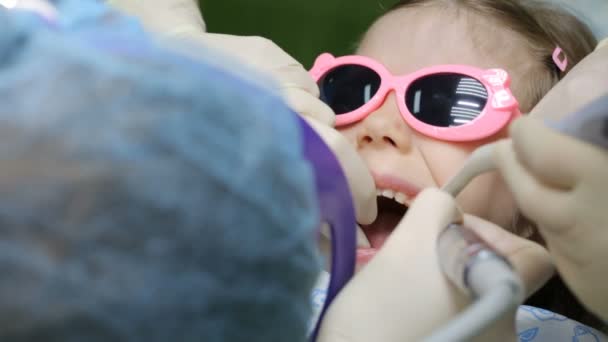 Маленькой девочке в стоматологическом кресле лечат зуб — стоковое видео