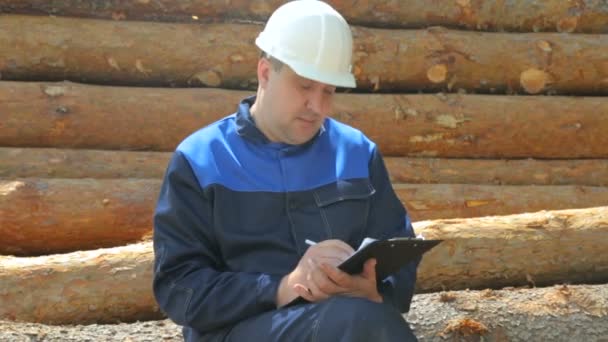 Arbeiter mit Unterlage sitzt auf Holzstapel — Stockvideo