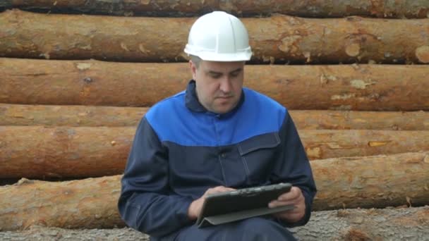 Trabajador con tablet PC sentado en un montón de troncos — Vídeo de stock