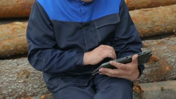 Рабочий с планшетным ПК сидит на куче бревен — стоковое видео