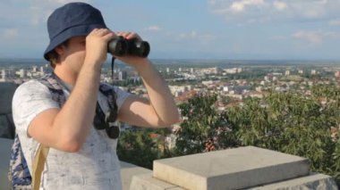 Şehrin yukarısında dürbünle bakan genç bir erkek turist.