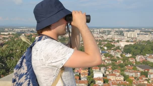 Mladý muž turista dívá dalekohledem nad městem — Stock video