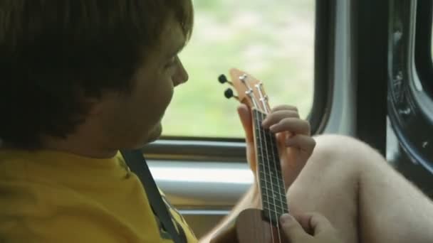 Молодий чоловік турист грає укулеле в машині — стокове відео