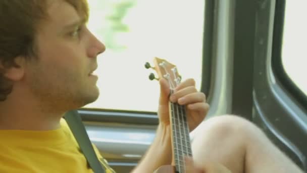 Young male tourist playing ukulele in car — Stock Video