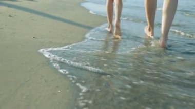 Kızıyla birlikte yaz günü sahilde yürüyen bir kadın.