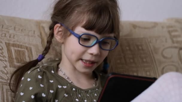 小さな女の子読みます電子本にソファに家 — ストック動画