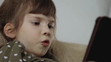 Evdeki koltukta elektronik kitap okuyan küçük bir kız.