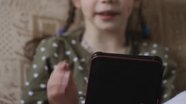 Little girl reading electronic book on couch at home — Stock Video