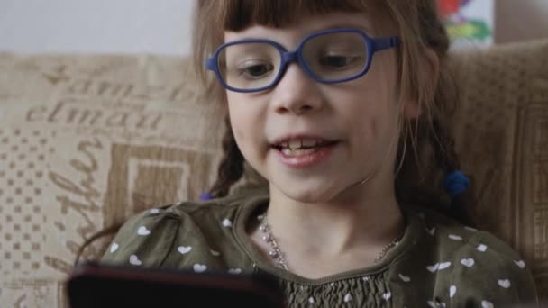 Маленька дівчинка читає електронну книгу на дивані вдома — стокове відео