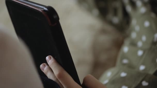 Petite fille lisant le livre électronique sur le canapé à la maison 