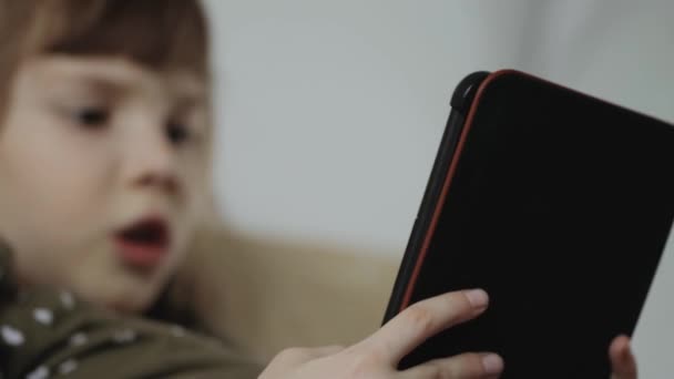 Маленька дівчинка читає електронну книгу на дивані вдома — стокове відео