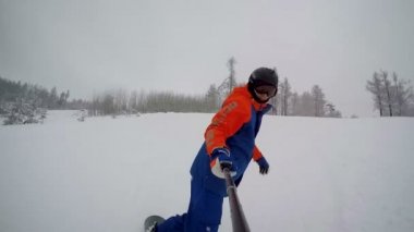 Snowboard sporcusu geniş bir yoldan dağdan aşağı iniyor. Selfie çubuğundan görüntü.