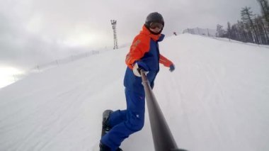 Bir snowboardcu yüksek hızla dağdan iner. Selfie çubuğundan ön manzara